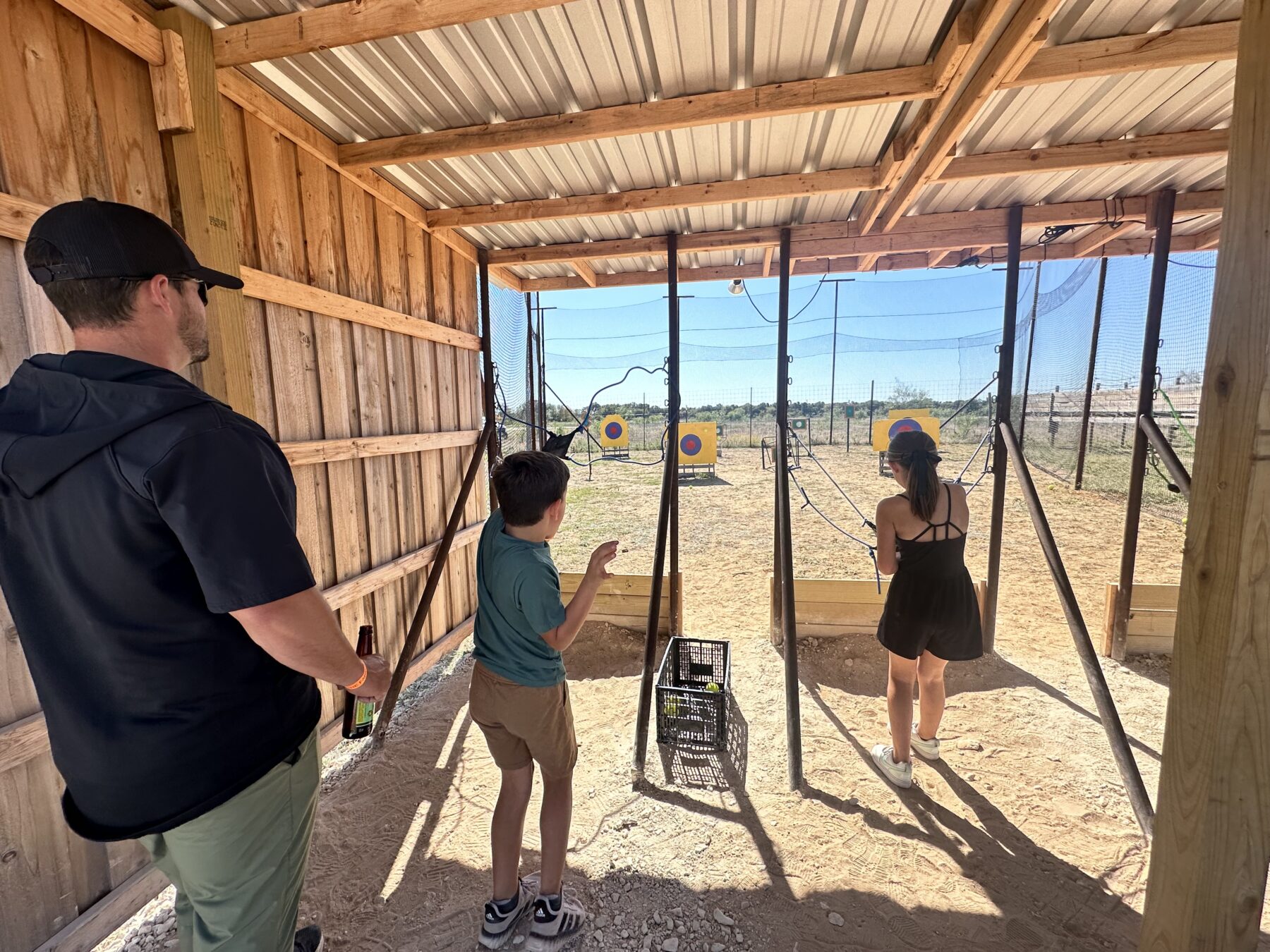 Kids practicing archery under a covered shelter at Denton Valley Farms near Clyde, Texas