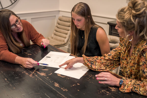 Three women discussing real estate documents at table.